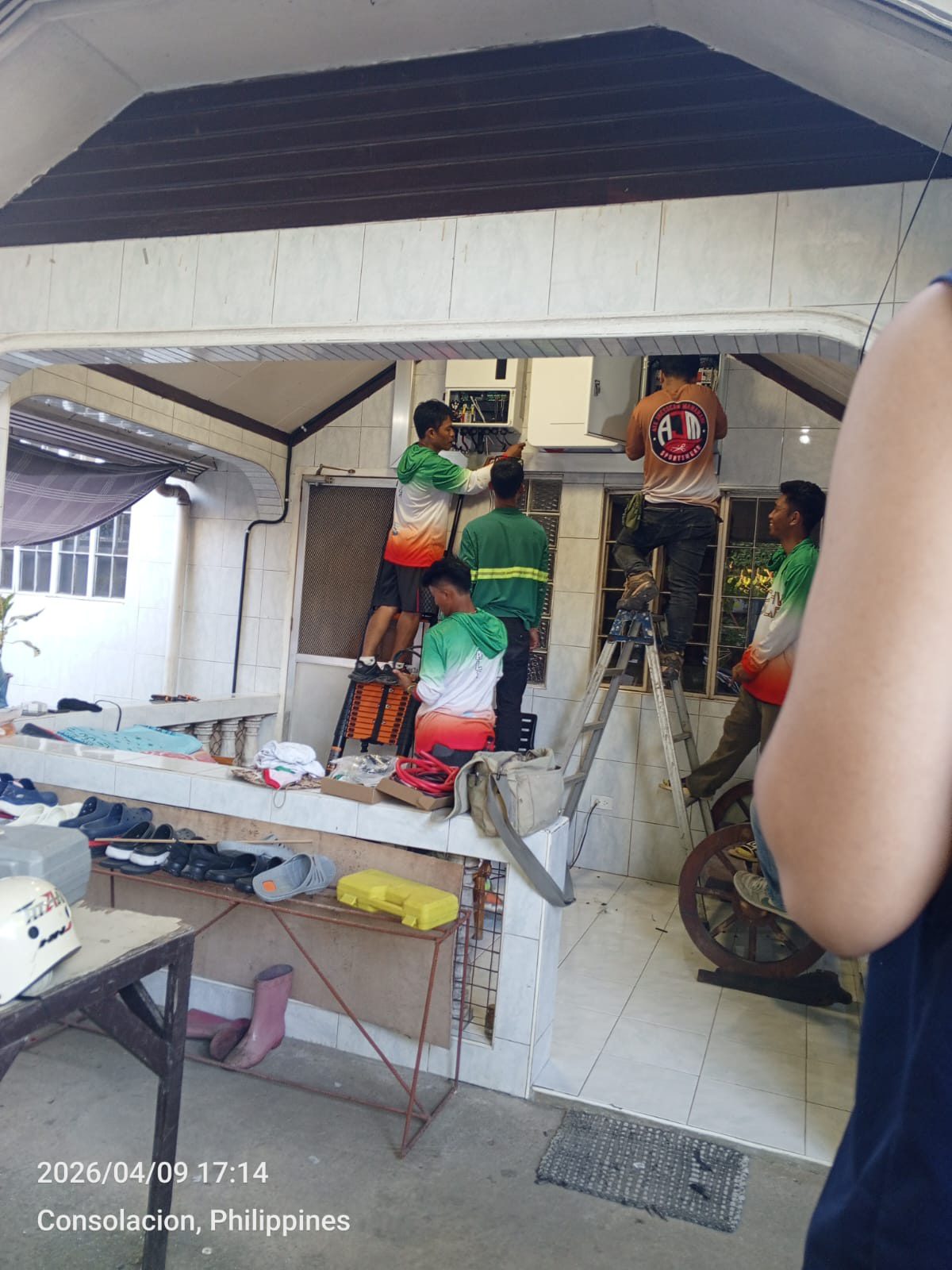 Four-person Achiv team mounting a split-type aircon indoor unit on a covered porch wall in Consolacion, a ladder and tools fanned out around them.