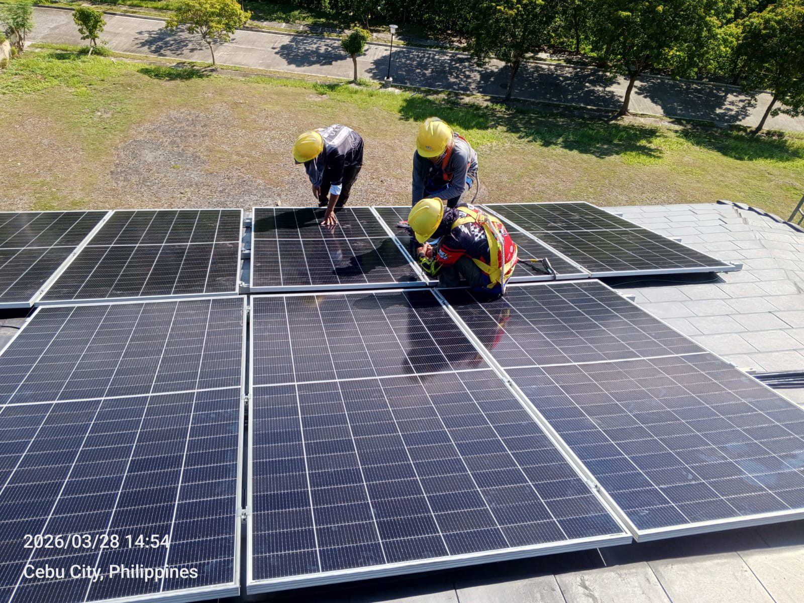 Three Achiv installers in hardhats kneeling on a flat dark Cebu City rooftop, mounting panels in even rows under a clear midday sky.